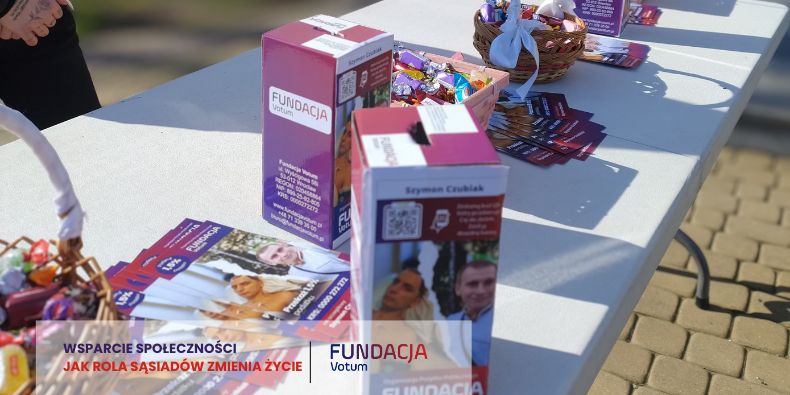 Outdoor charity table with Fundacja Votum materials: purple donation boxes, brochures, flyers, and a wicker basket of promo items on a white table.