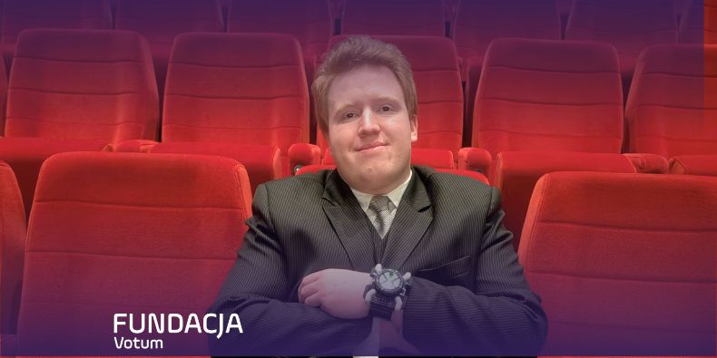 Man in a suit sits with folded arms in a red theater, with a Fundacja Votum watermark in the corner.