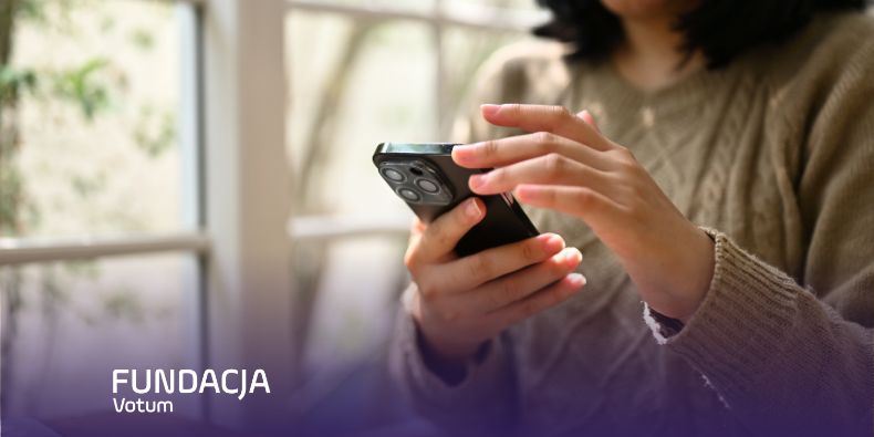 Person in a beige sweater uses a smartphone indoors by a window; Fundacja Votum logo appears in the bottom-left corner.